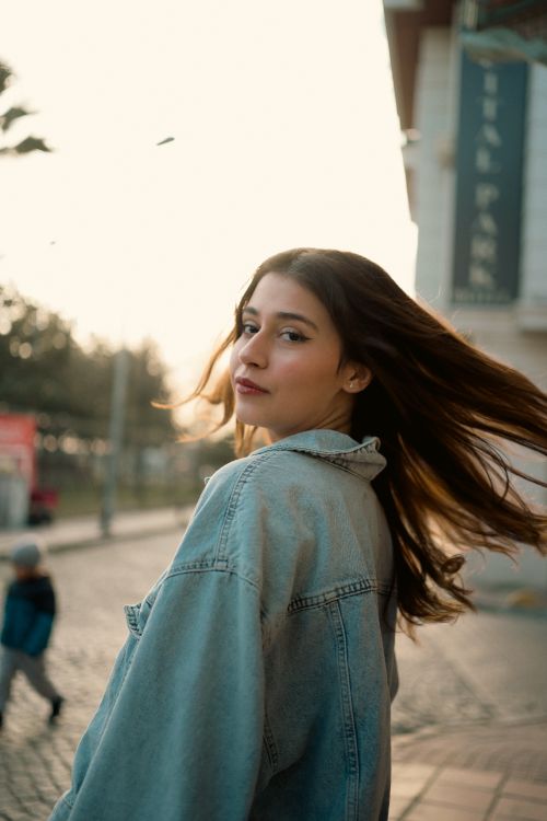 Free Portrait of a young woman in a denim jacket on a street at sunset. Stock Photo