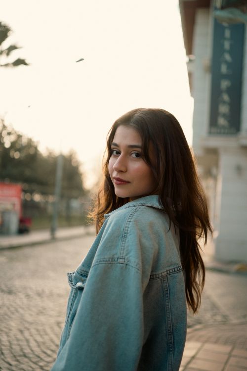 Free Young woman with brown hair in a denim jacket on a city street. Warm, evening ambiance. Stock Photo