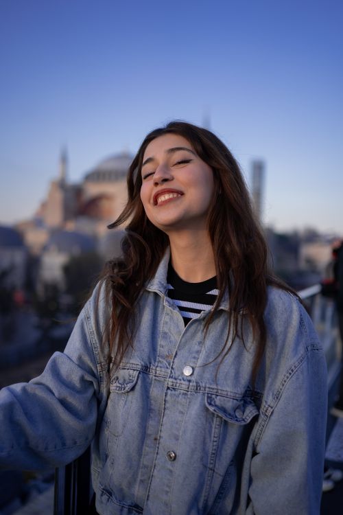 Free Smiling young adult in denim jacket, iconic landmark in background, twilight setting. Stock Photo