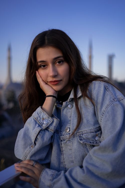 Free Young woman in denim jacket posing at twilight with a scenic backdrop. Stock Photo