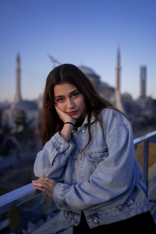 Free A young woman in denim poses pensively in front of a mosque at twilight, capturing serenity. Stock Photo