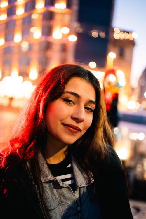 Free Portrait of a young woman smiling against a vibrant city night backdrop. Stock Photo
