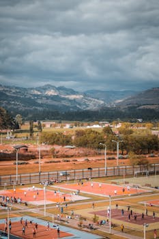 在多云天空下，网球场与球员的空中镜头以令人惊叹的山景为背景