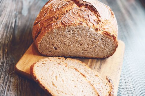Free Freshly baked rustic whole wheat bread loaf with slices on a wooden board. Stock Photo