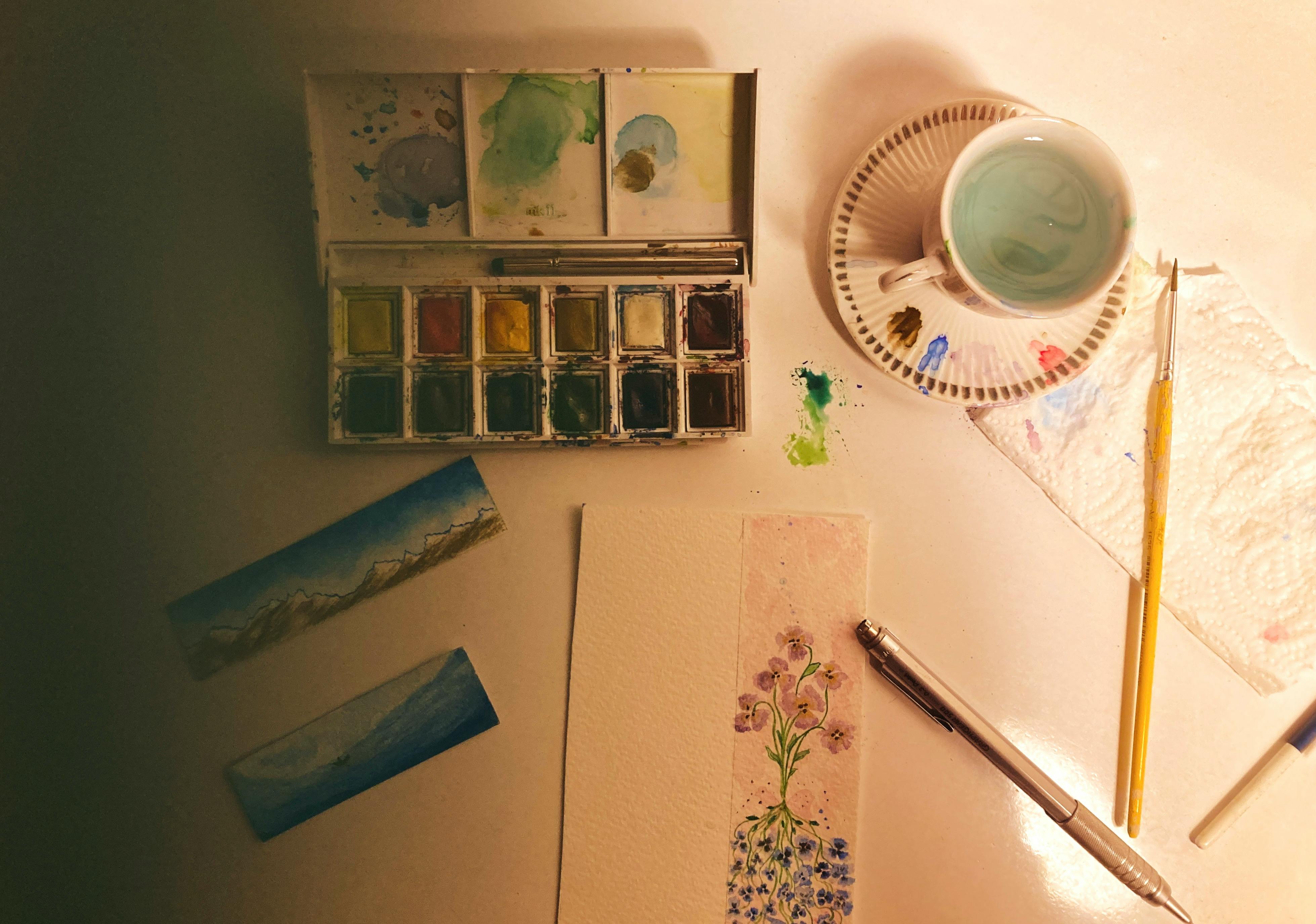 A creative watercolor art setup with paints, brushes, and paper featuring floral designs.