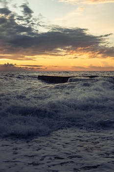 Waves crashing against a pier at sunset, creating a dramatic seascape view.