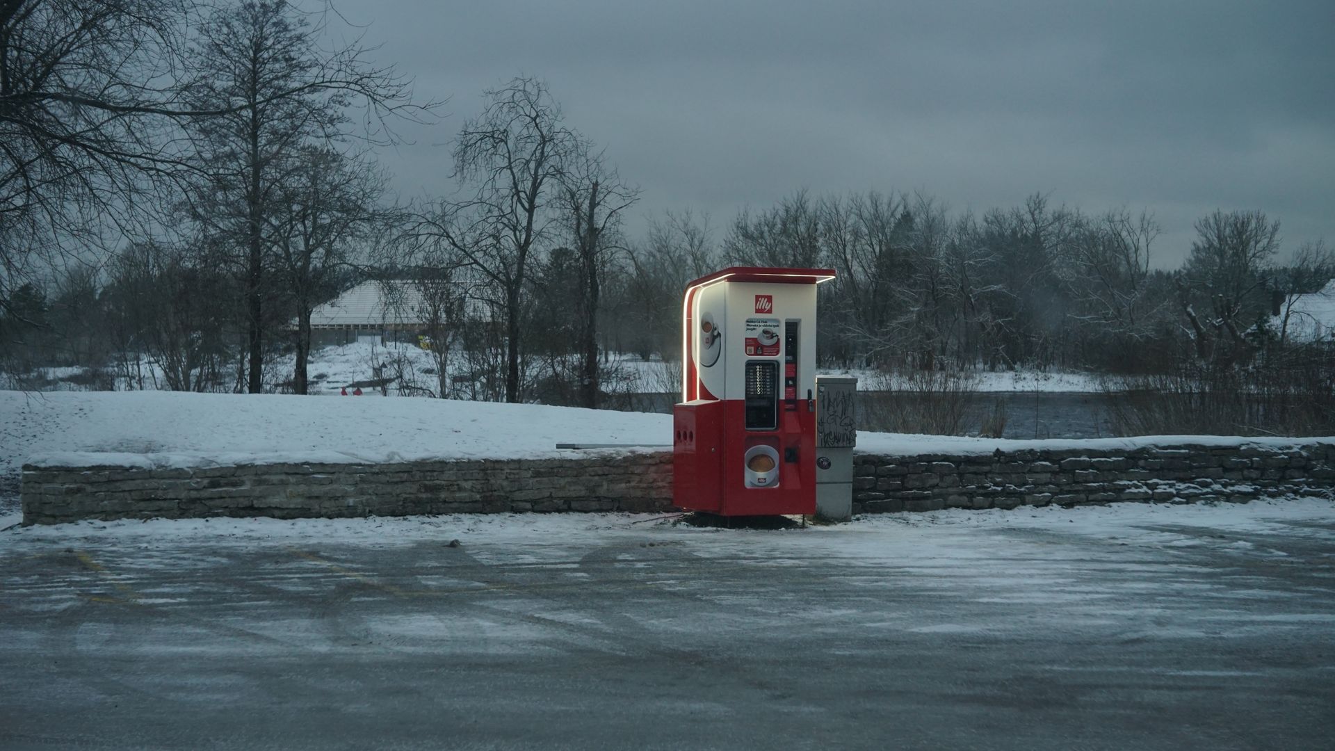 A lonely coffee vending machine in a winter landscape with snow-covered grounds.