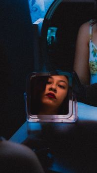 A mysterious portrait of a woman with red lipstick reflecting in a small mirror with dramatic lighting.