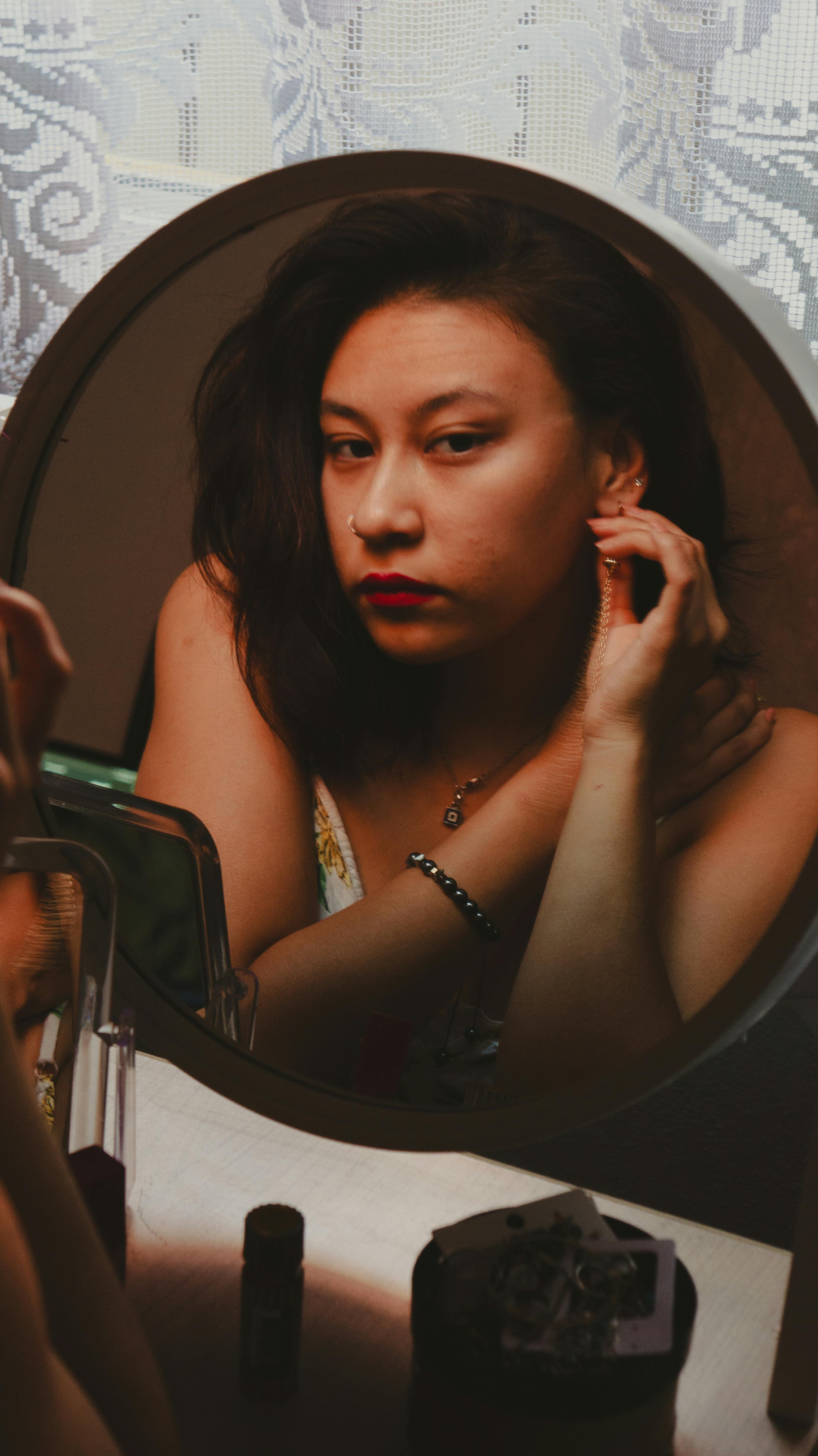 A woman in front of a mirror adjusting her earring, captured indoors.