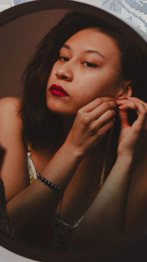 Free A woman applies earrings and makeup in a moody indoor setting. Stock Photo
