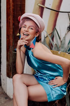 一位时尚的年轻女子身着活力蓝色连衣裙，头戴别致帽子，在户外微笑着摆好姿势拍照