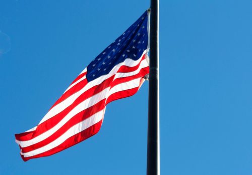 Free American flag gracefully waving on a flagpole against a clear blue sky, symbolizing patriotism. Stock Photo
