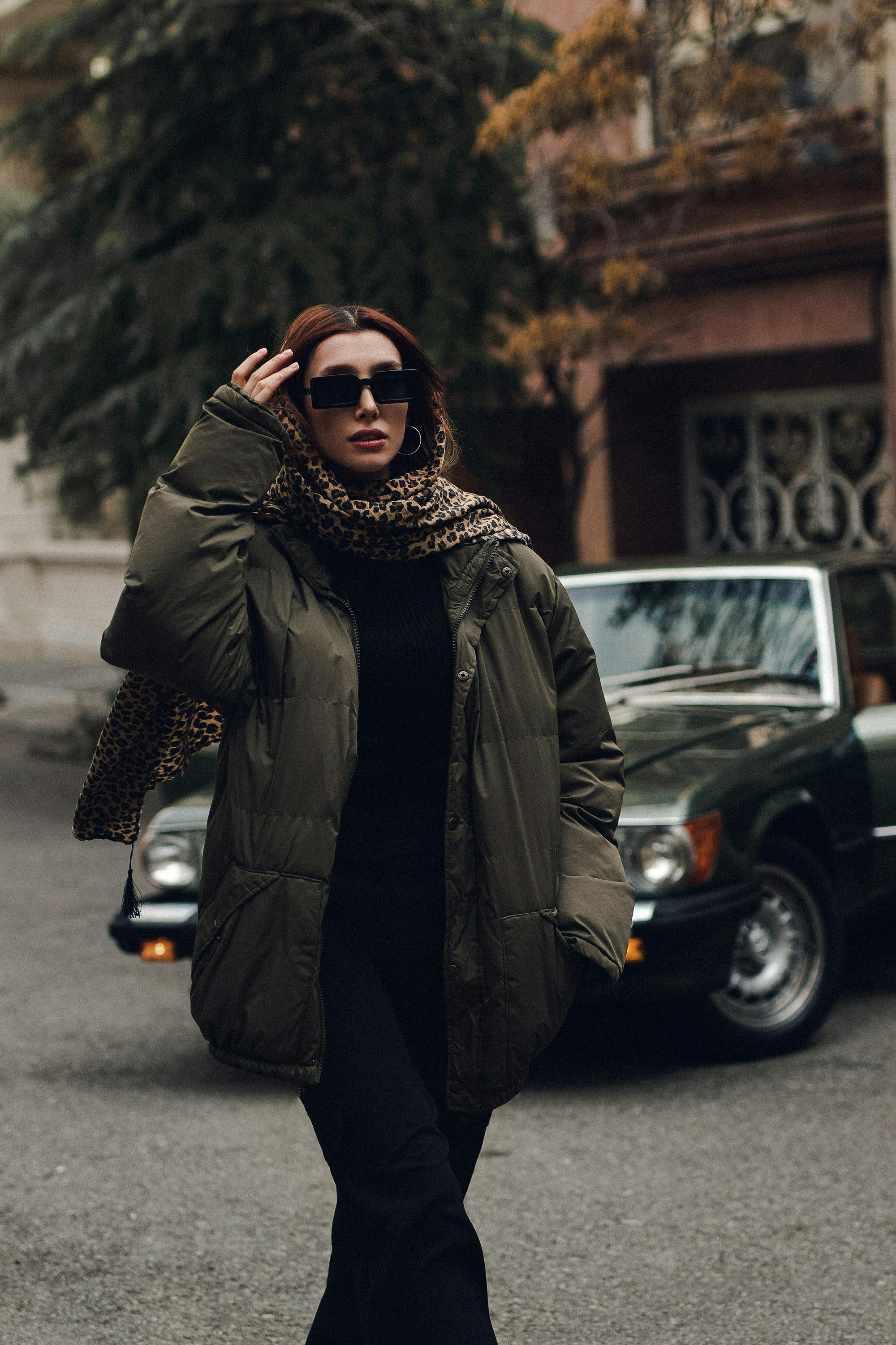 grátis Mulher elegante em traje de inverno posando confiante em ambiente urbano com óculos escuros e cachecol. Foto profissional