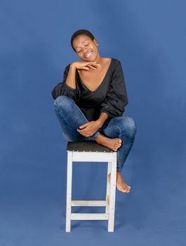 A woman sitting comfortably on a stool against a blue background, exuding relaxation.