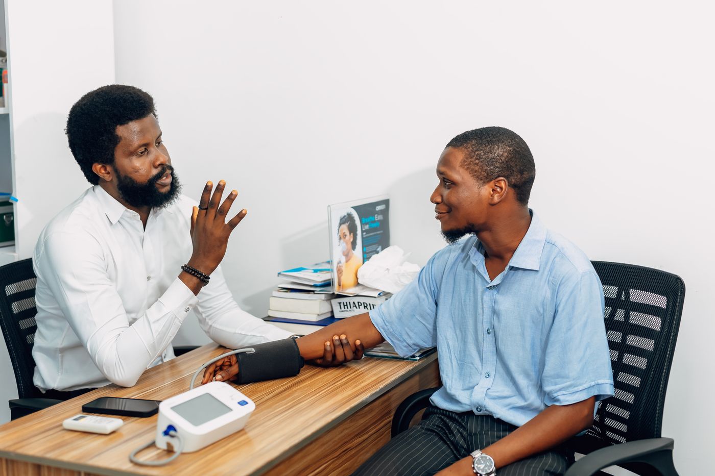 A Black doctor talking warmly with a patient during a checkup in a bright office