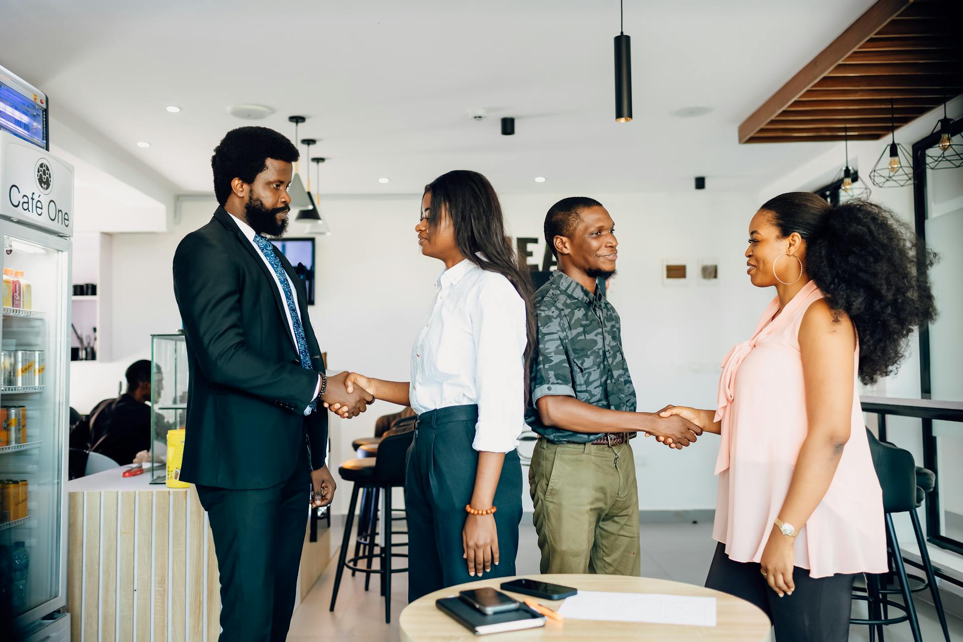 A group of four business people, two men and two women, are in a cafe standing, shaking hands and talking.  Find more afro-centric images at www.ninthgrid.com