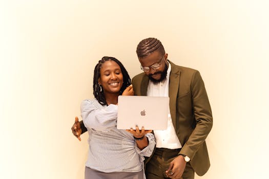 Two colleagues smiling while collaborating on a laptop in an office setting.