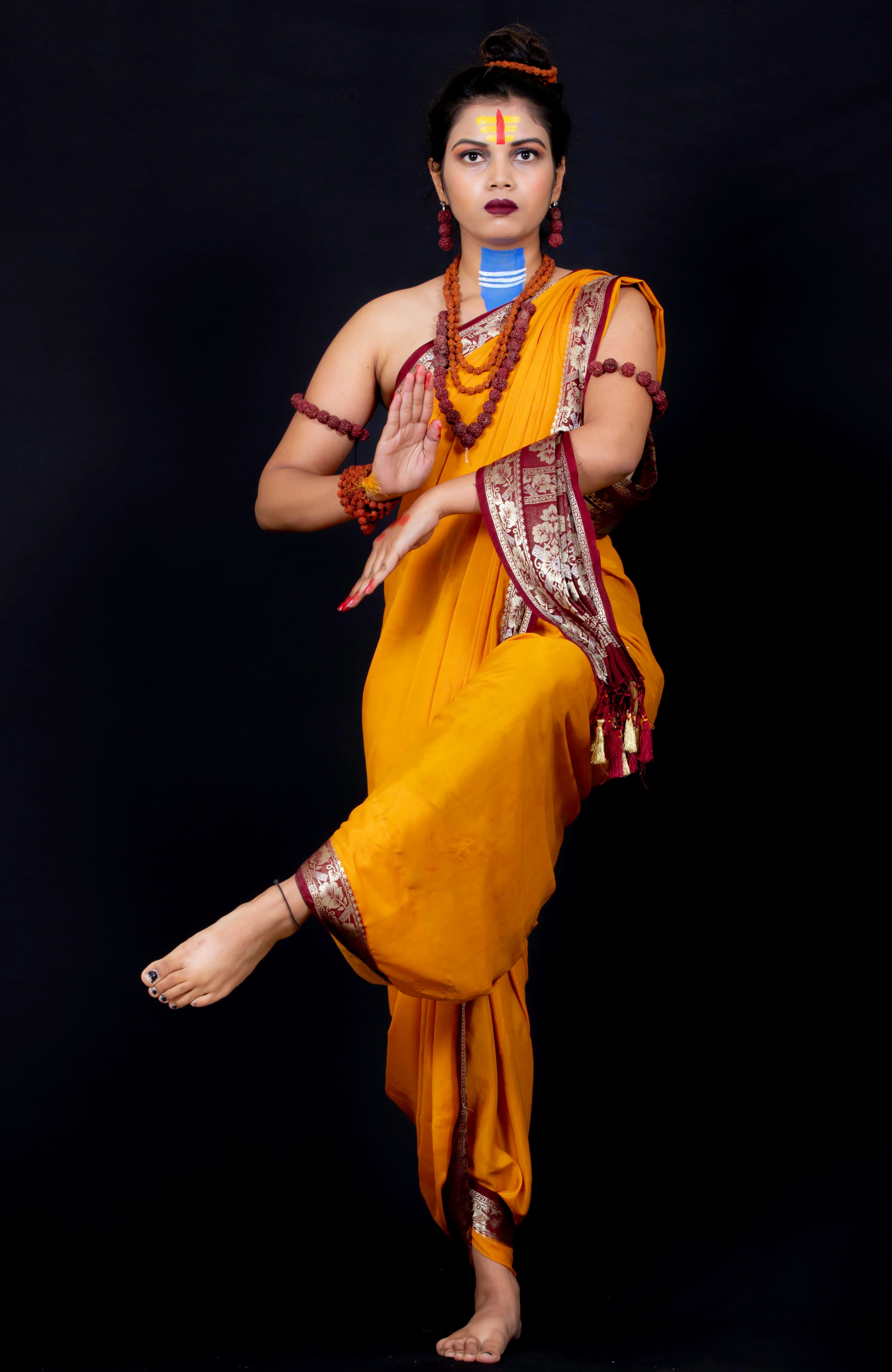 Woman in traditional Indian attire performing classical dance pose against black background.