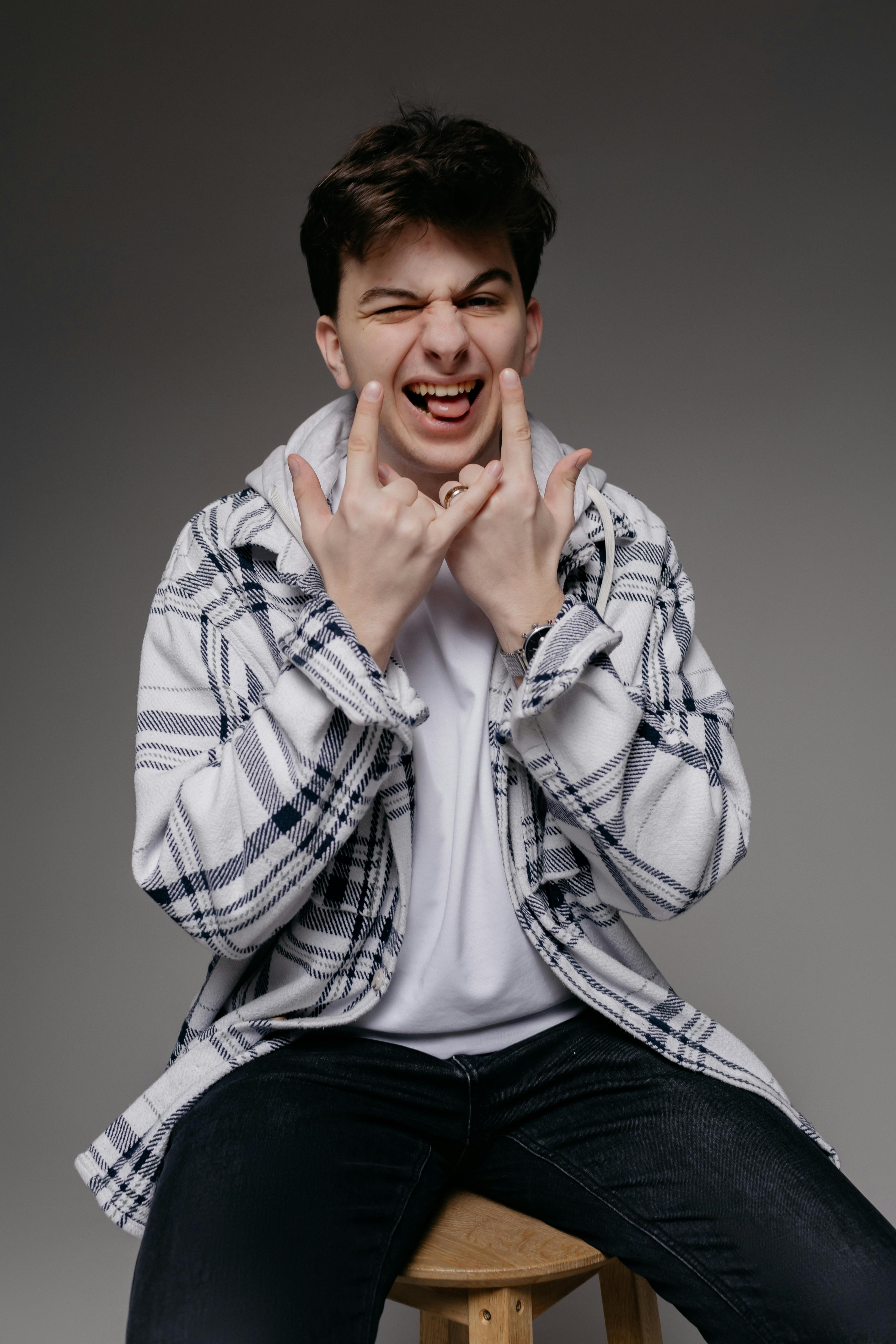 bezplatná Hravý mladý muž v ležérní kostkované košili dělá obličeje v prostředí studia. Základová fotografie