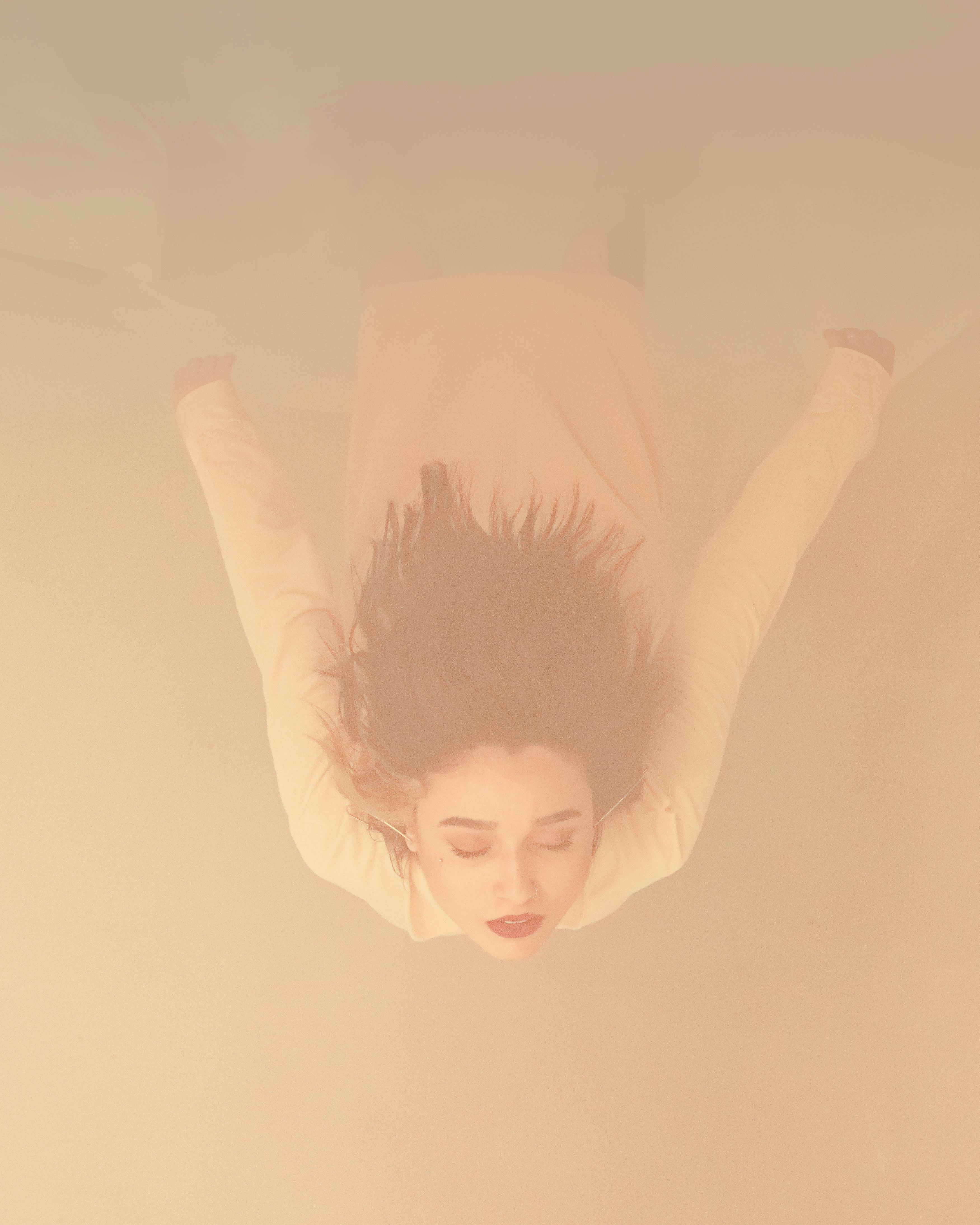 一张色彩柔和的艺术照片中，一名女子漂浮在水下