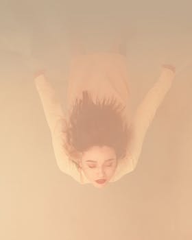 一张色彩柔和的艺术照片中，一名女子漂浮在水下