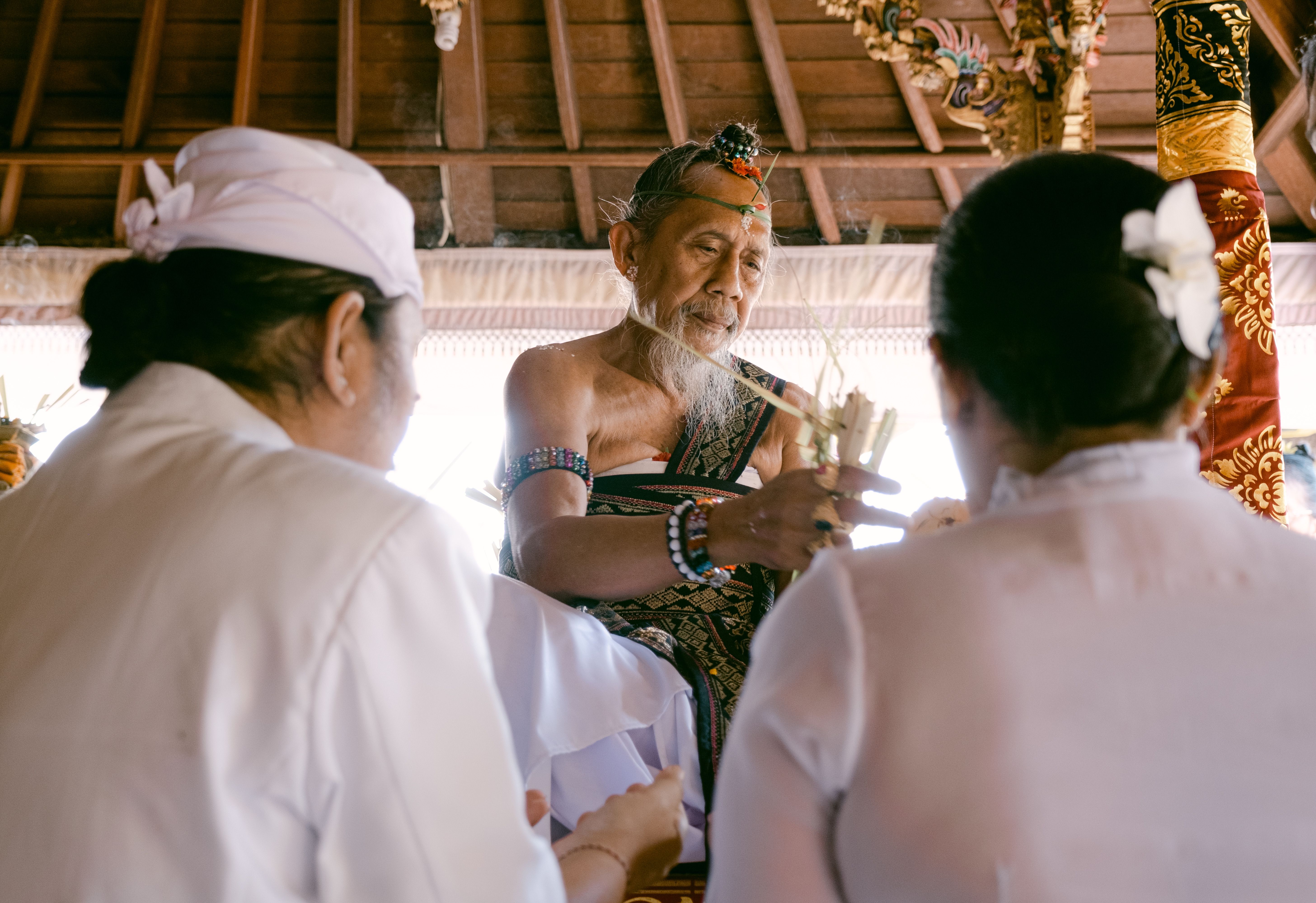 Balinese priest performing traditional ceremony, two people observing.
