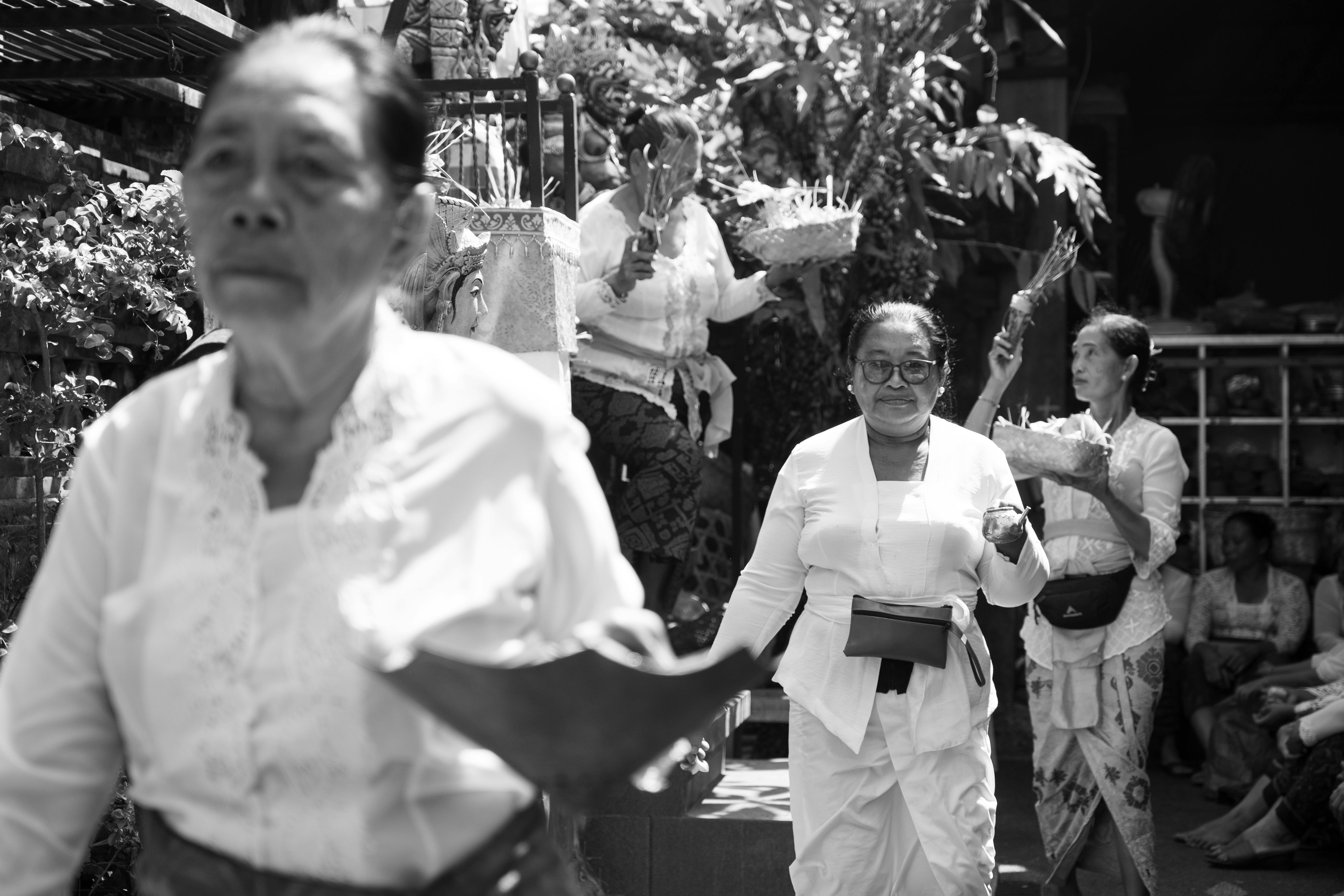 Women in traditional attire participate in a Balinese ceremony outdoors.