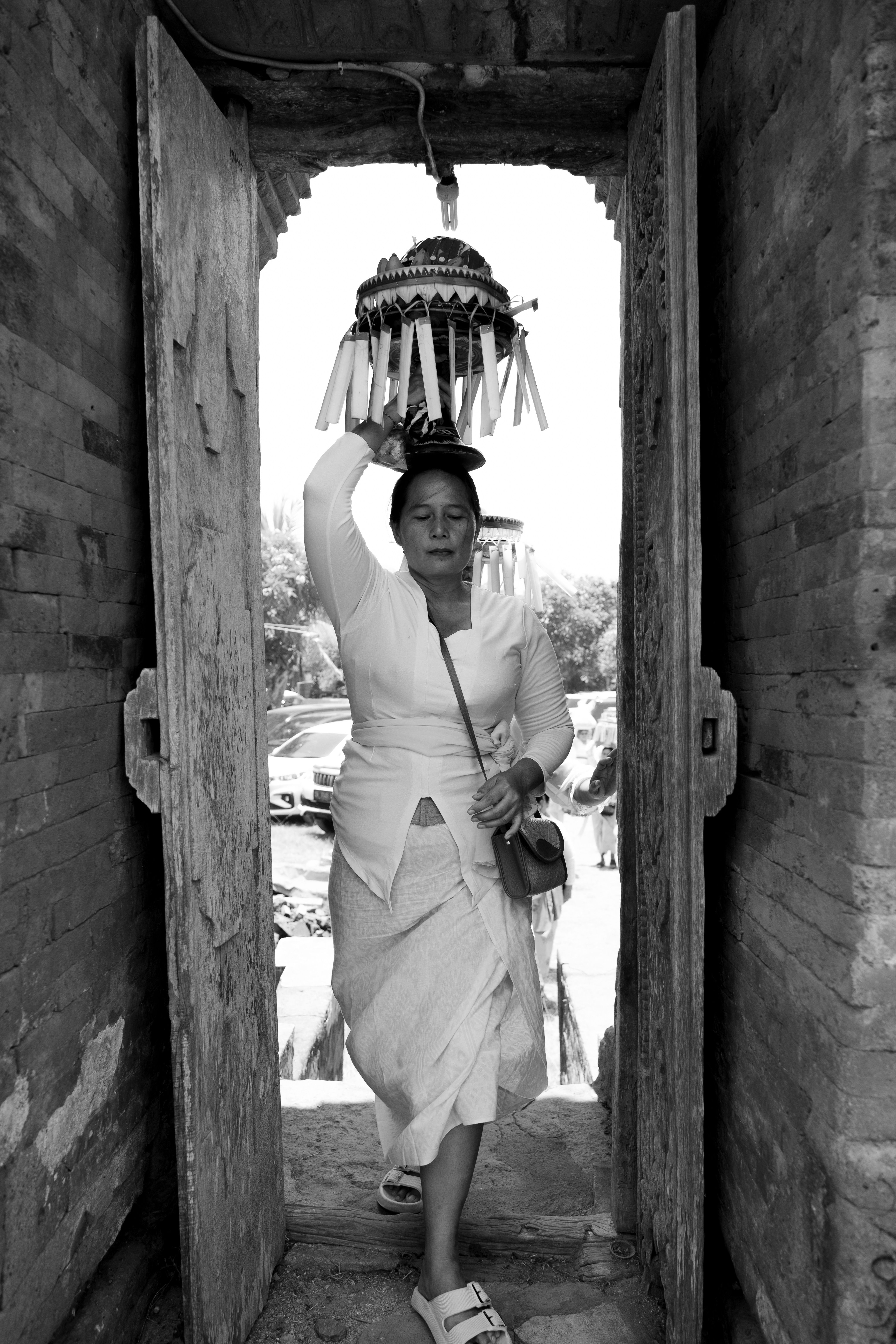 A woman in traditional dress carries ceremonial items through an ancient temple doorway.