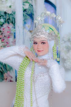 Elegant Indonesian bride in intricate white attire with ornate headdress, posing gracefully.