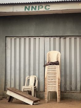 Stack of plastic chairs beside a closed metal door with NNPC label on building facade.