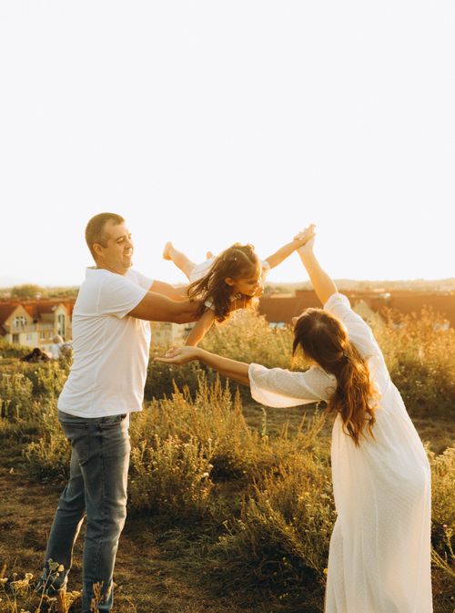Free A happy family playing together in a sunny field during sunset. Stock Photo