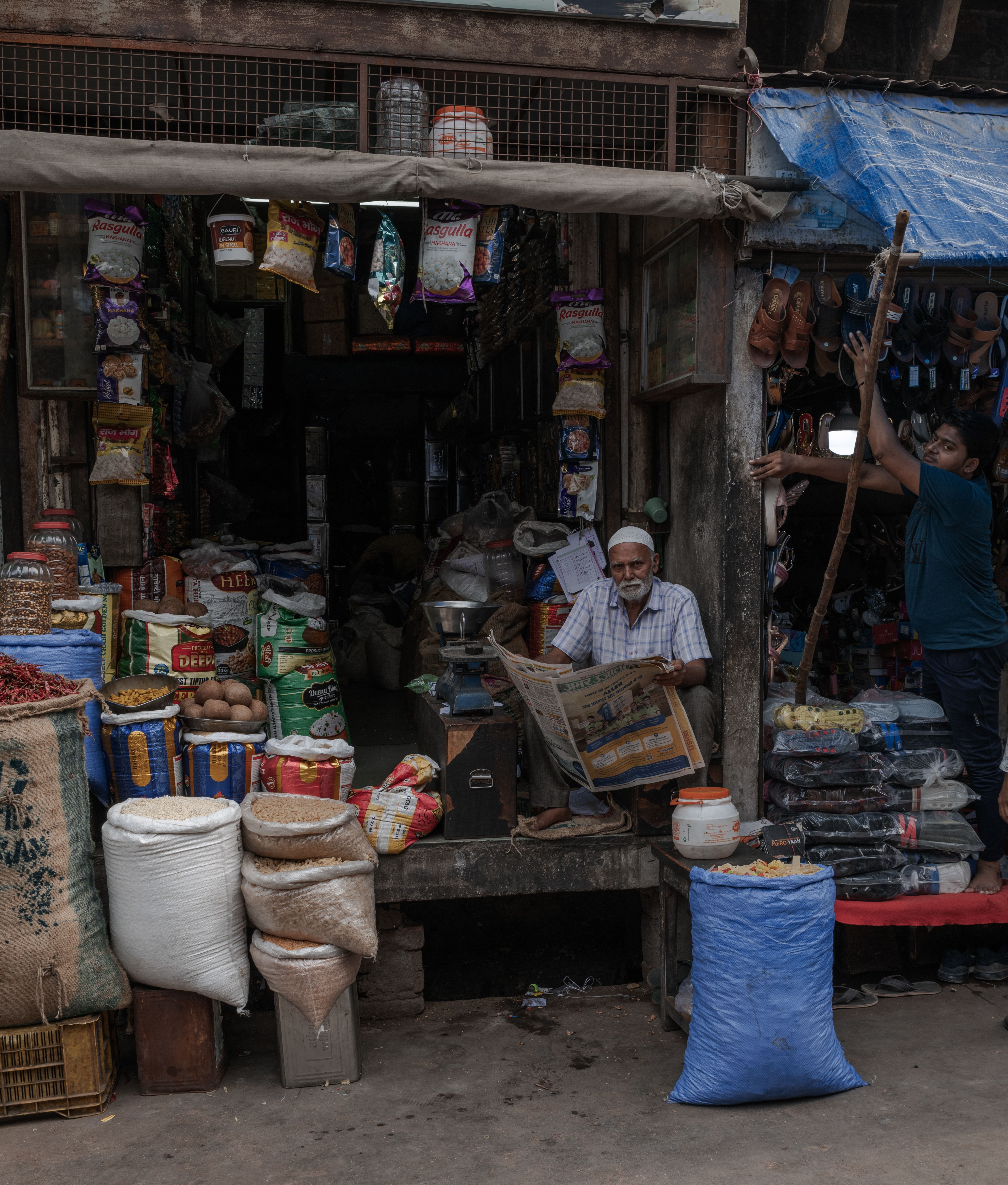 A bustling spice shop in Mathura, displaying bags of spices and an elderly vendor reading a newspaper.