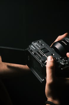 Detailed shot of a filmmaker's hands holding a professional camera in moody lighting.
