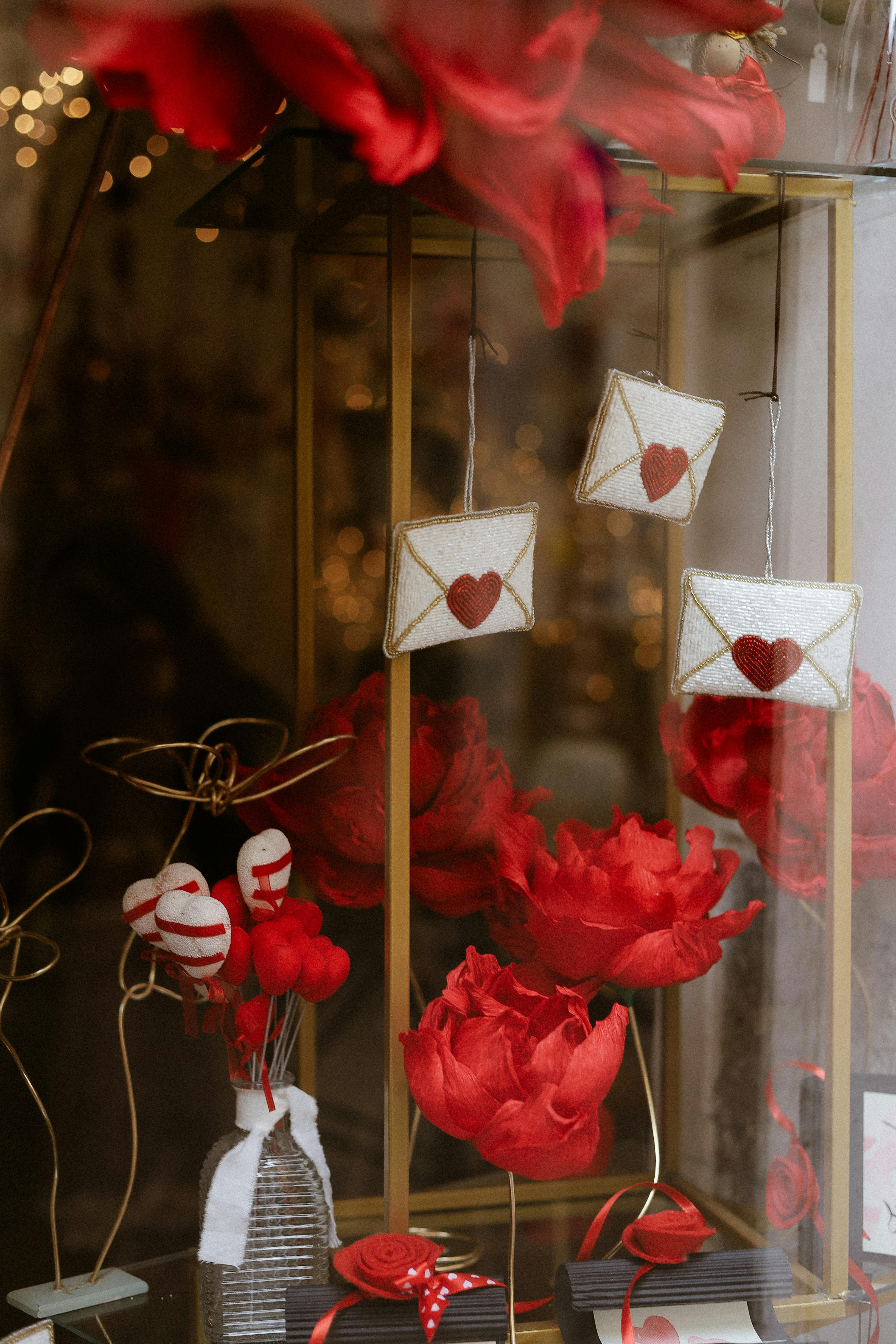 Romantic display with red roses, heart decorations, and love letters in a window.