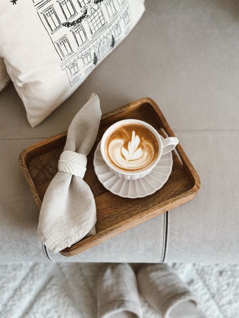 Cozy latte in wooden tray with napkin and pillow background, perfect for relaxing moments.