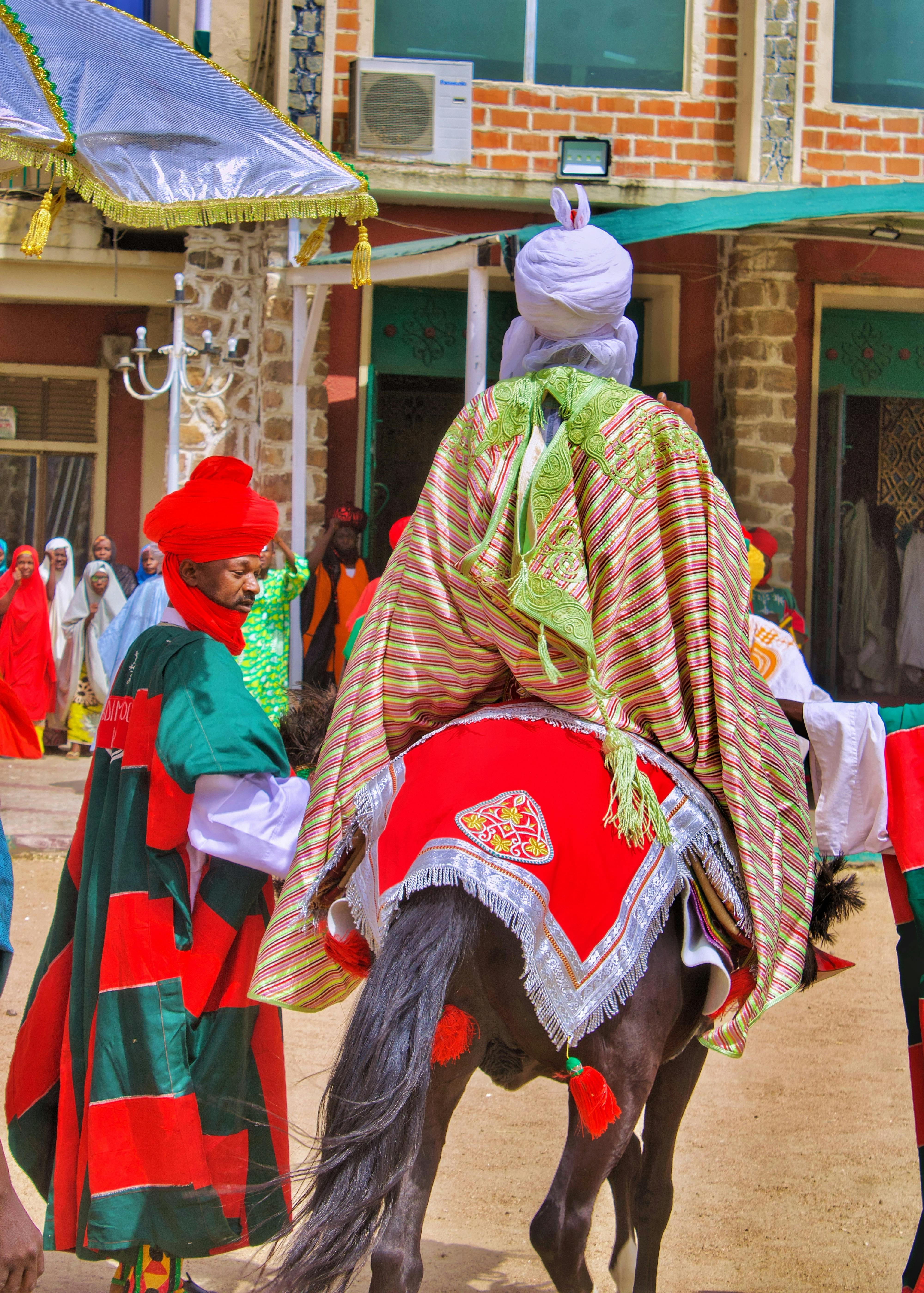 Colorful display of traditional Nigerian attire during a parade in Kano, Nigeria, featuring riders and vibrant costumes.