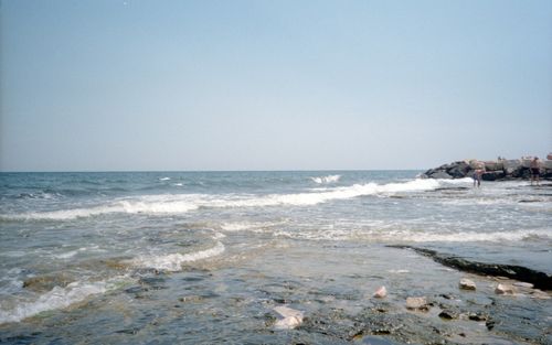 Free Calm sea waves gently crashing on a rocky shoreline under a clear blue sky. Stock Photo