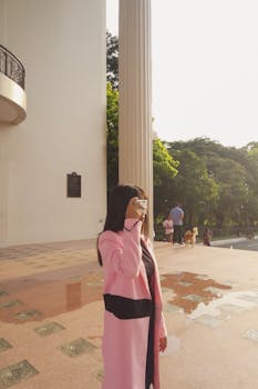 一名身穿粉色外套的女子正在一座古典建筑附近拍摄风景优美的户外区域