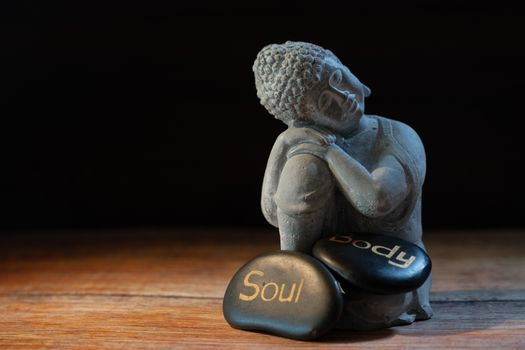 Buddha statue with stones labeled 'Soul' and 'Body', symbolizing mindfulness and balance.