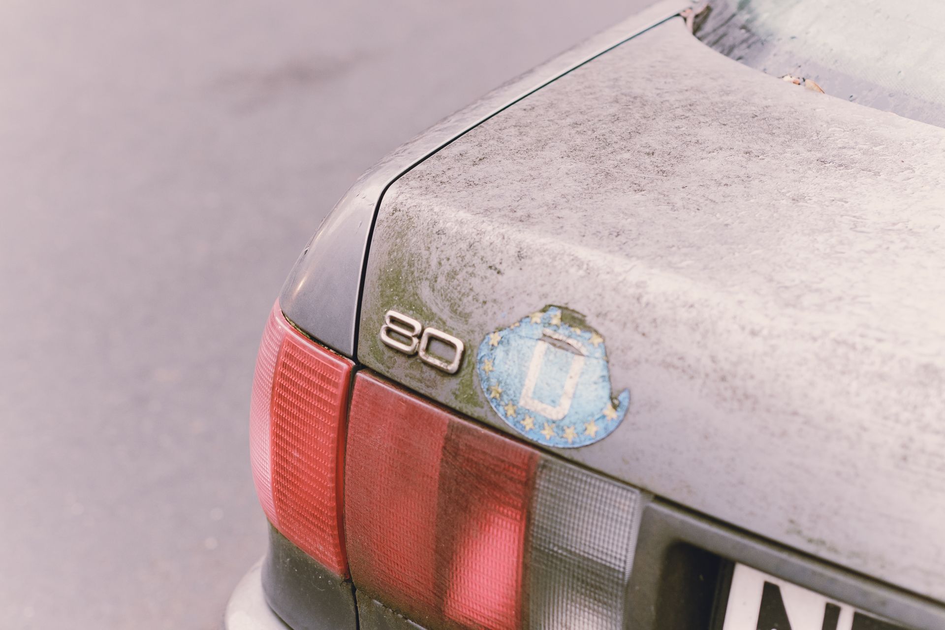 Close-up of a dusty vintage car trunk featuring a European Union sticker and distinctive tail light.