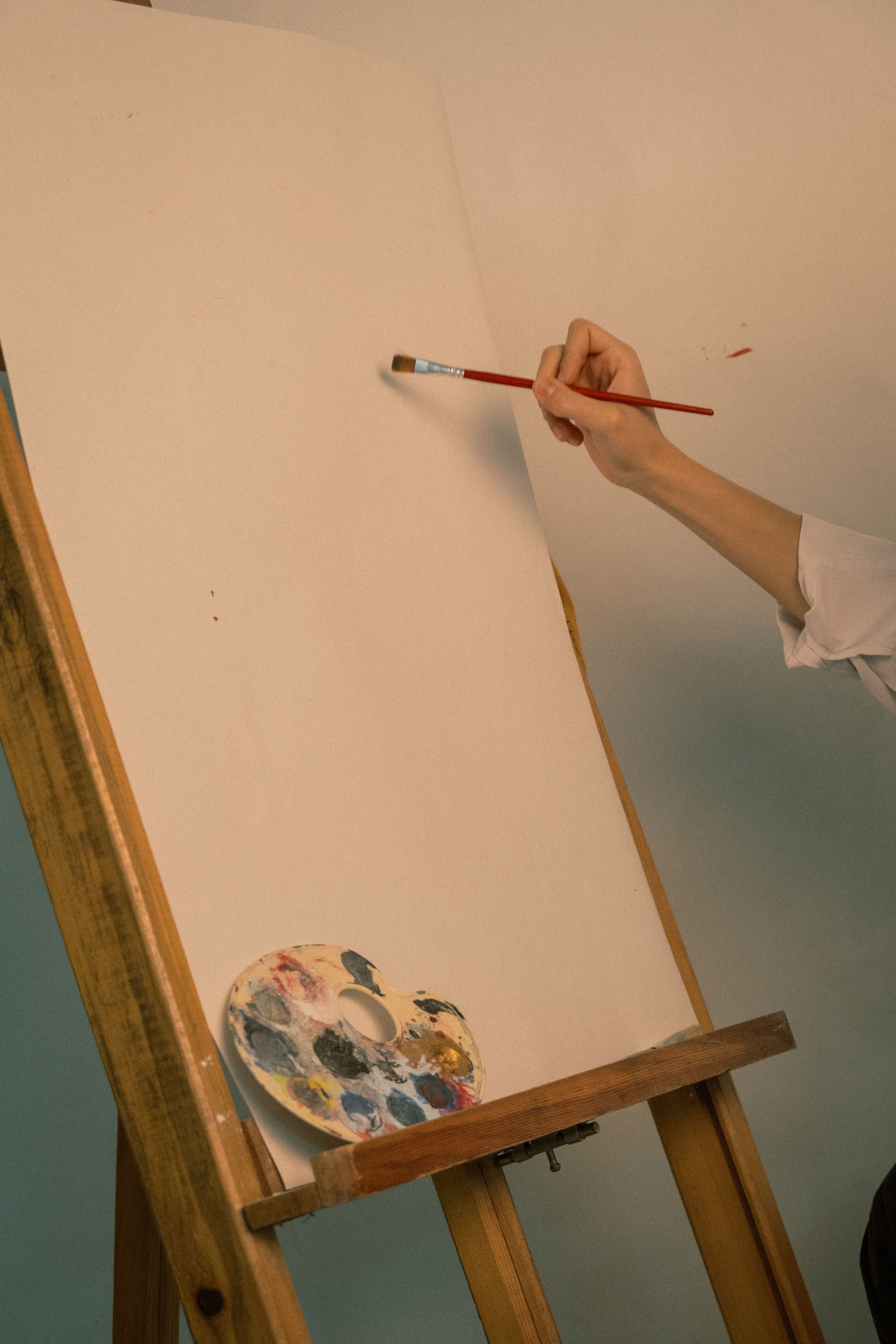 An artist's hand begins painting on a blank canvas with a paintbrush, evoking creativity.