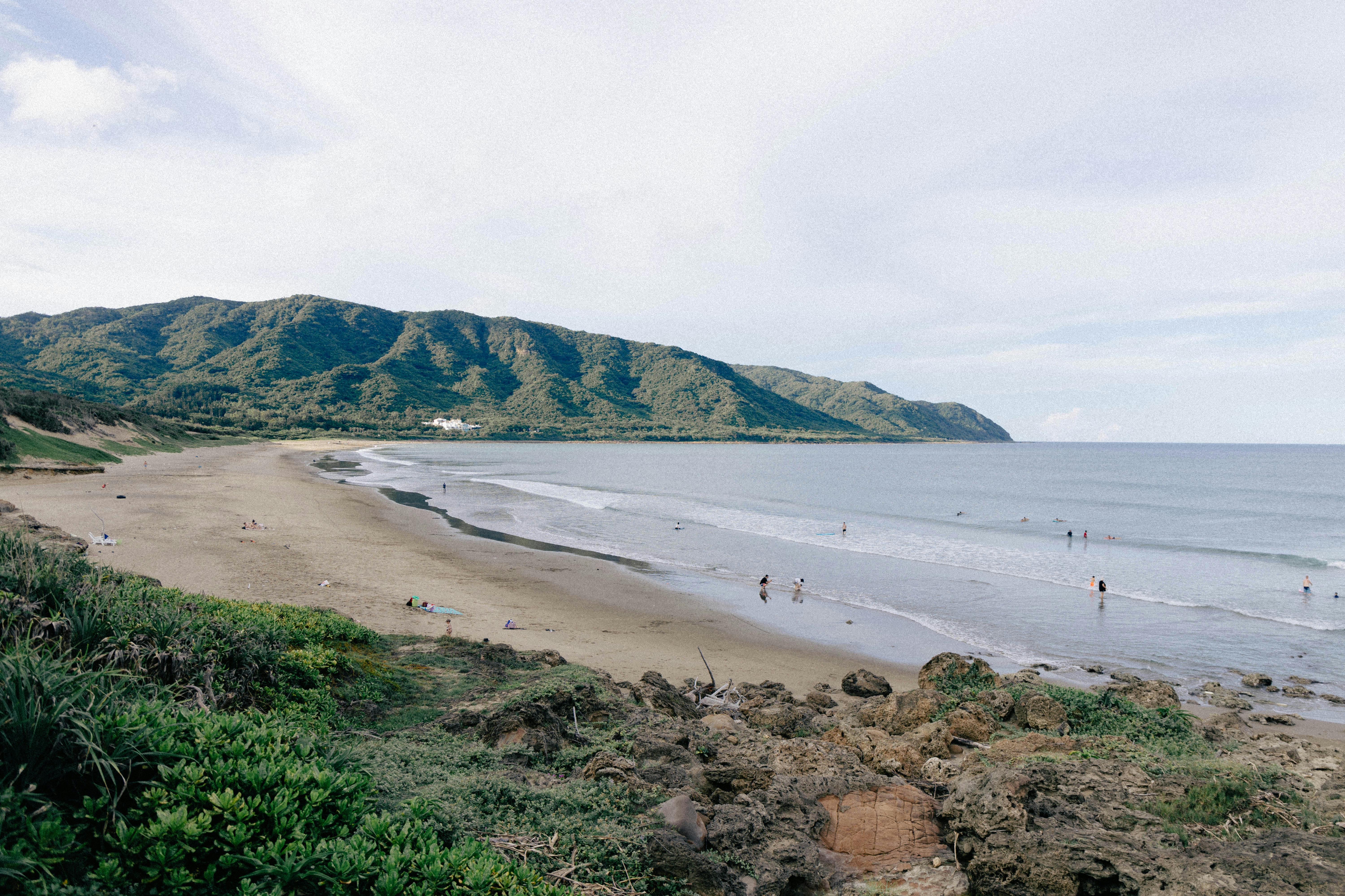 A tranquil beach scene on Taiwan's coast with gentle waves and lush mountains.