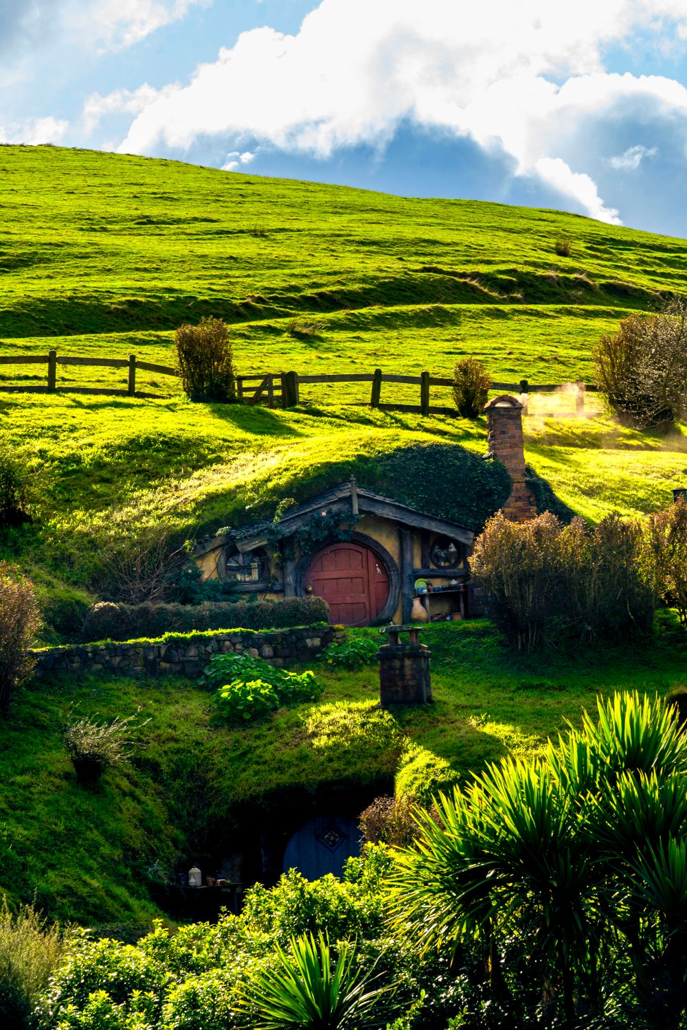 Casa hobbit con puerta roja y chimenea sobre la colina verde de Hobbiton en Matamata