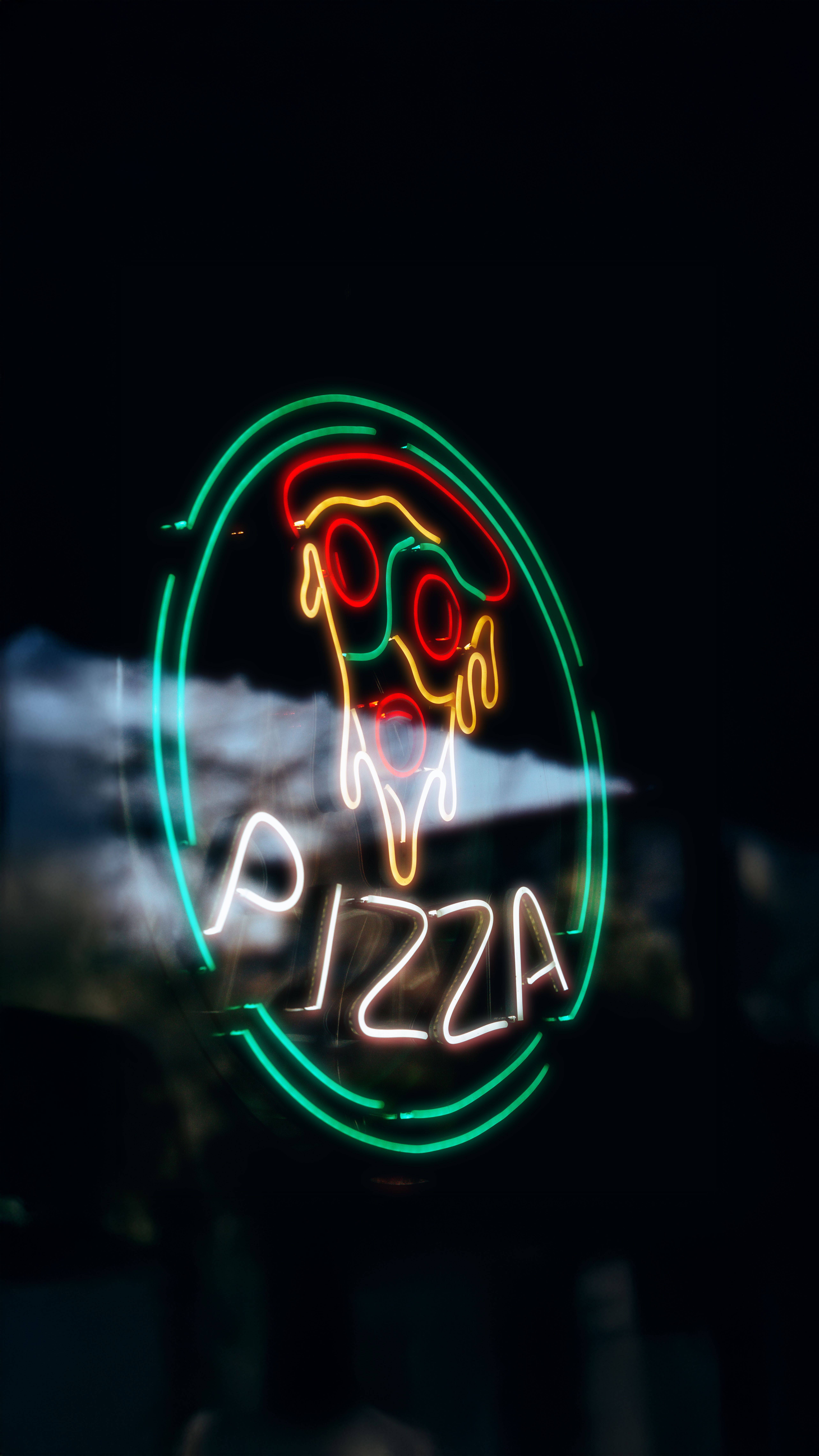 Colorful neon pizza sign glowing at dusk, creating a lively urban atmosphere.