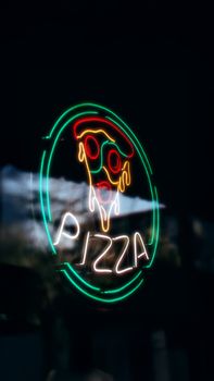 Colorful neon pizza sign glowing at dusk, creating a lively urban atmosphere.