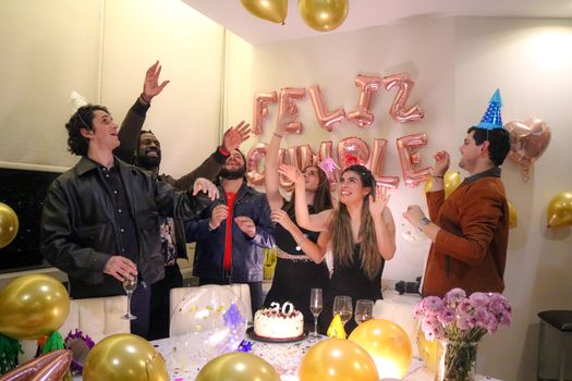Group of friends celebrating a birthday indoors with balloons and cake.