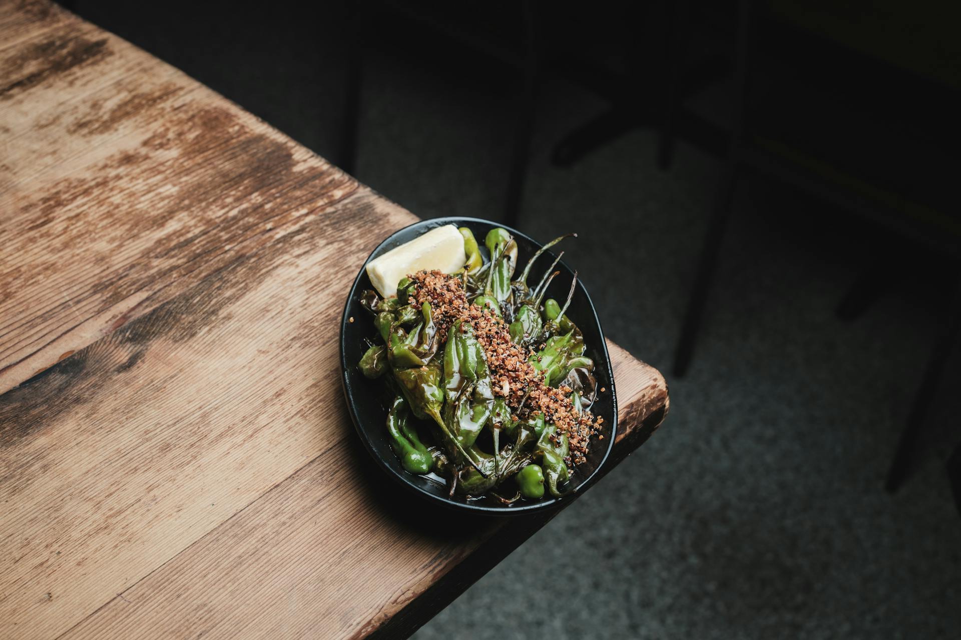 A plate of seasoned shishito peppers served on a rustic table, perfect for Japanese cuisine enthusiasts.