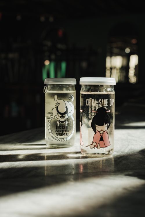 Free Two artistic sake cups with unique designs lit by sunlight on a table. Stock Photo
