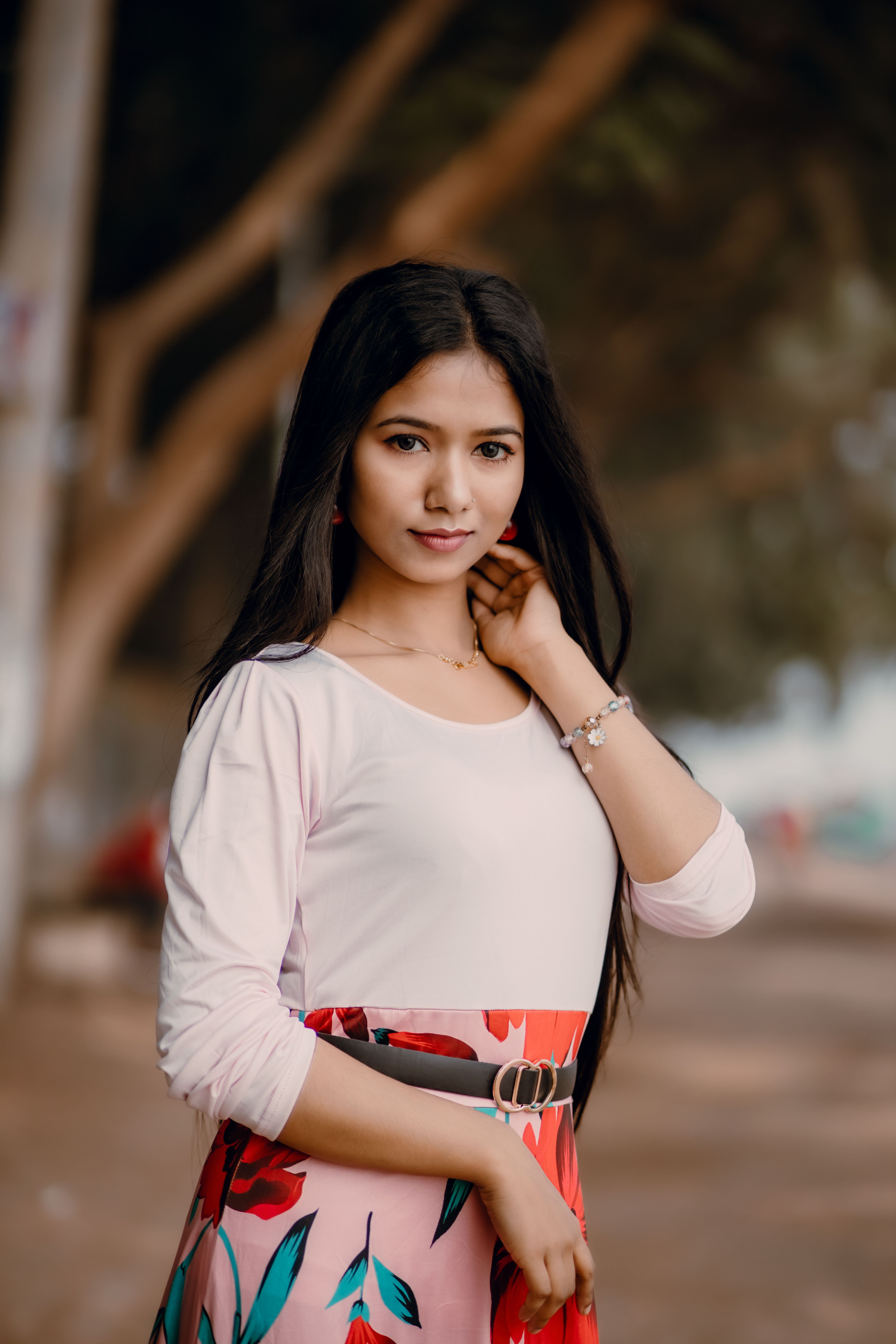 Portrait of a young woman outdoors wearing a floral skirt and white top, looking confidently at the camera.