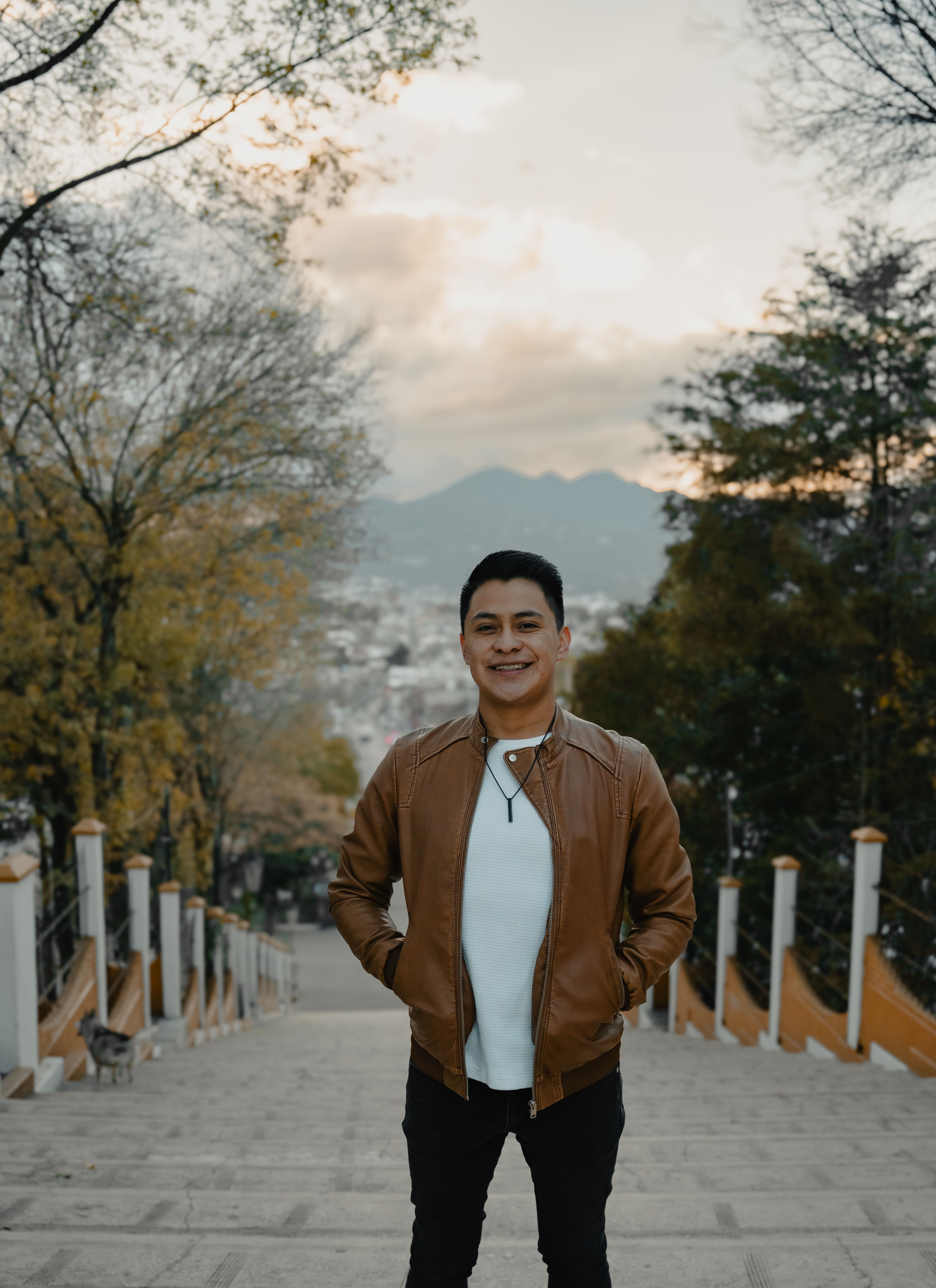 Man smiling on stairs in San Cristóbal de las Casas, surrounded by trees and mountains.